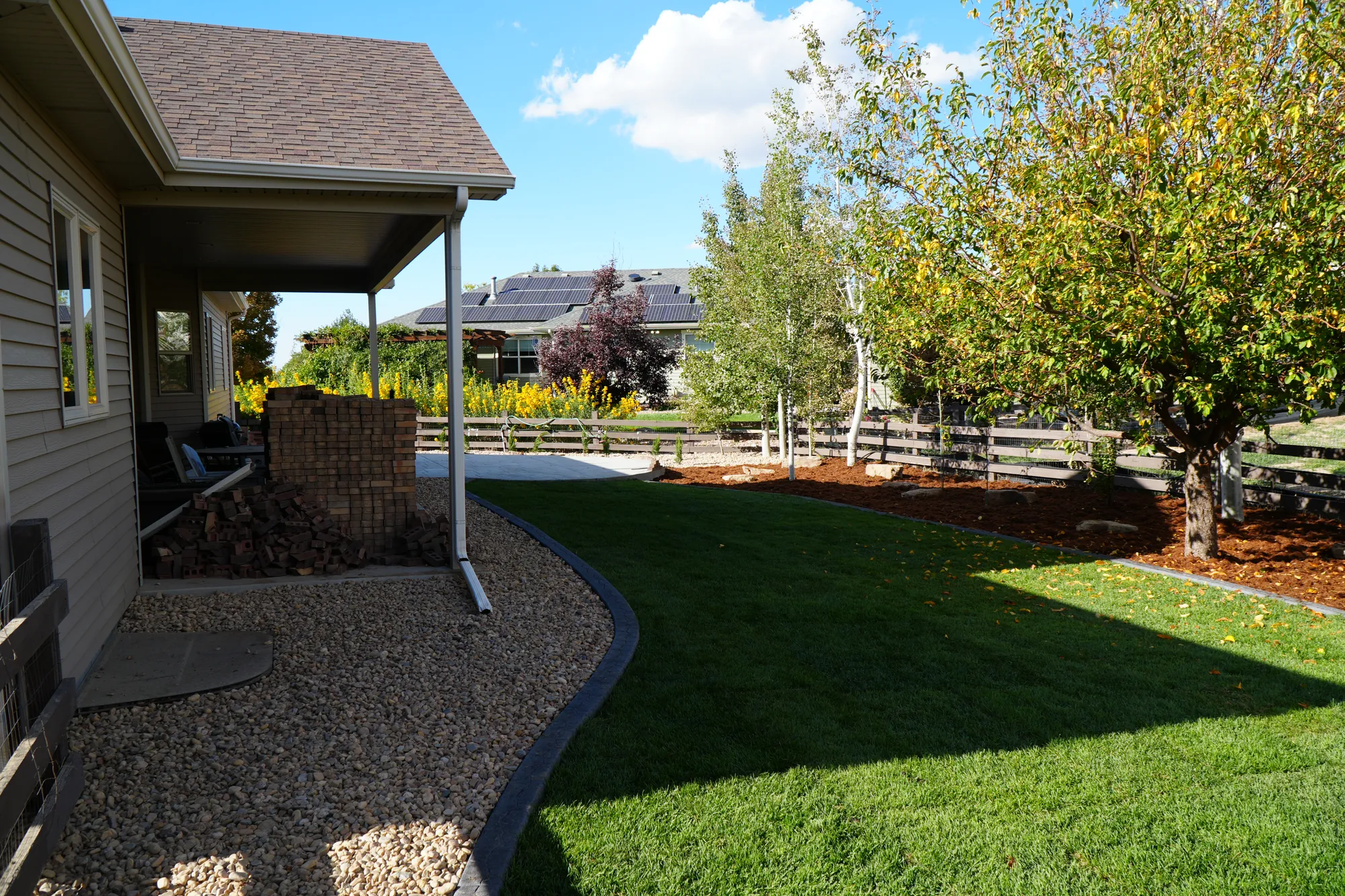 Backyard Landscaping: backyard lawn with a river rock strip running alongside the patio