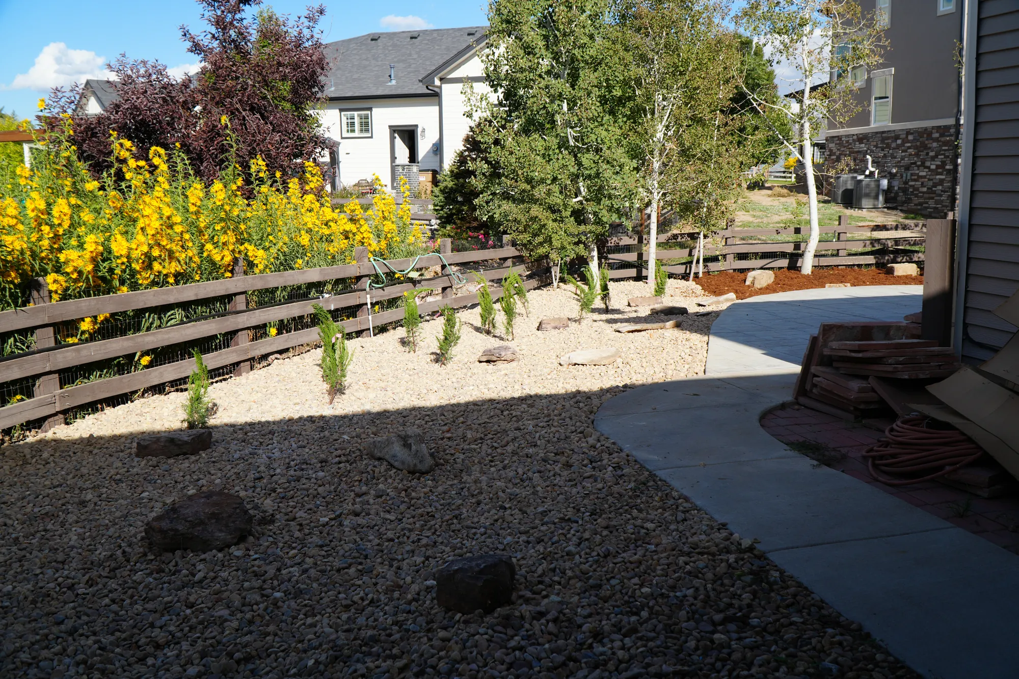 Xeriscape: low-water rock landscaping with boulders and shrubs along the fence line