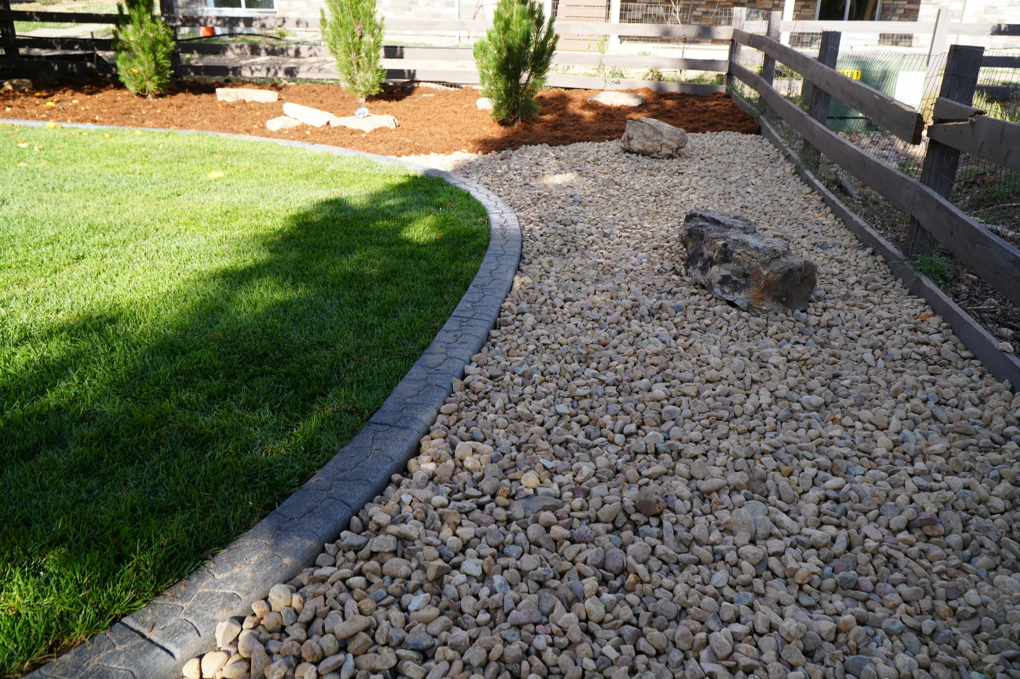 Rock Landscaping: river rock strip with curbing between the lawn and the fence