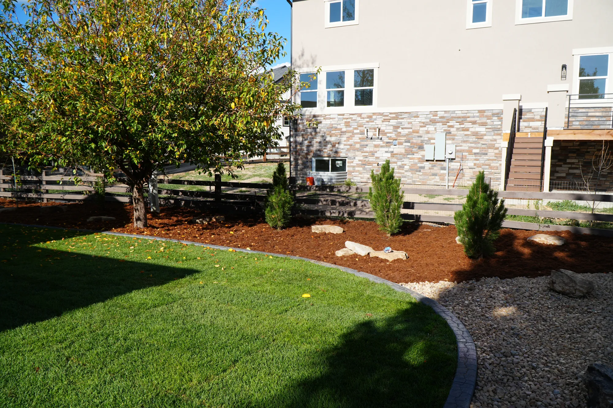 Backyard Landscaping: green lawn edged with concrete curbing and a river rock border